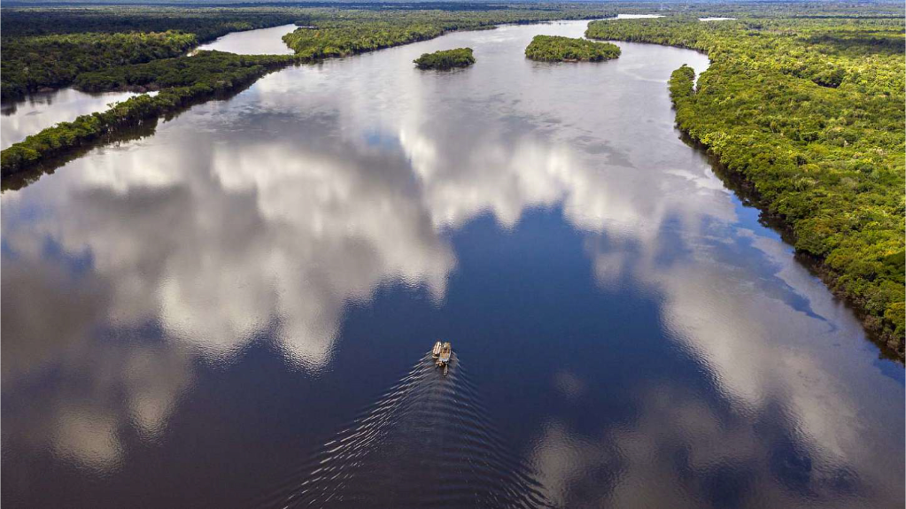 Imagem do Rio Amazônia com um barco pequeno navegando pelas águas. O barco, comparado ao tamanho do rio fica menor ainda.