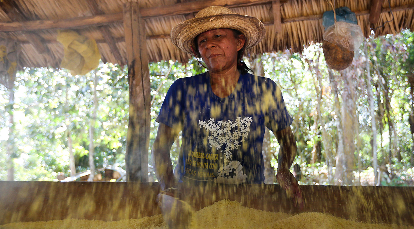 Imagem com mulher com um chapéu de palha, trabalhando com grãos na floresta.