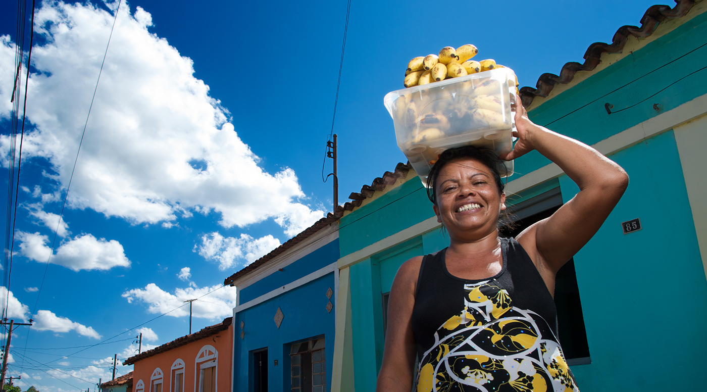 Mulher sorrindo com balde na cabeça com cachos de banana dentro dele.